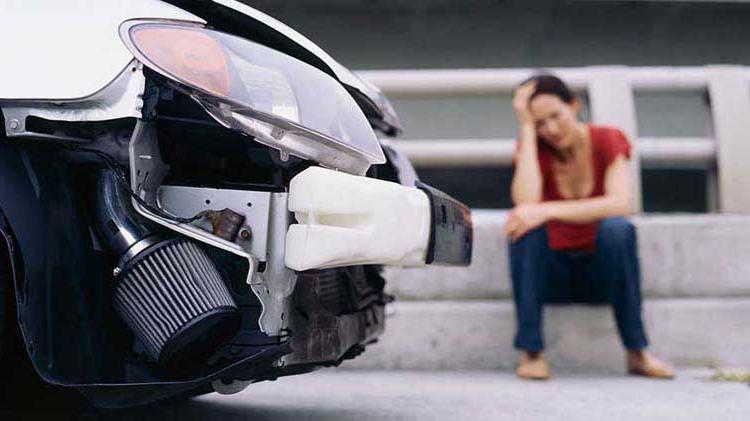 An upset woman sits next to a wrecked car.